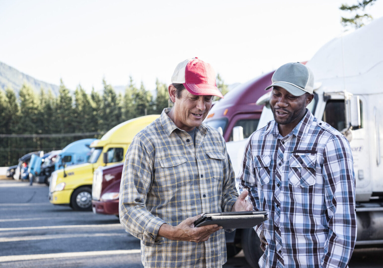 A caucasian man and a black man truck driving team together in a truck stop parking lot.